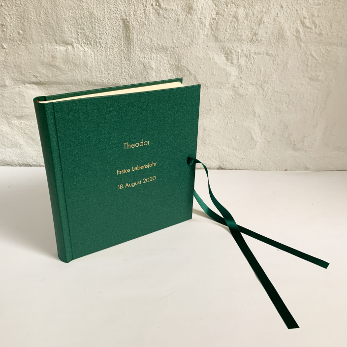 Edles Kinderfotoalbum in Waldgrün mit kleiner und großer Futura in Gold und Schleife.